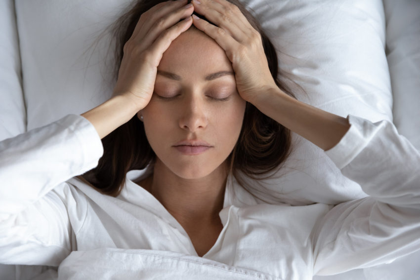 woman suffering from migraine headache, lying in bed